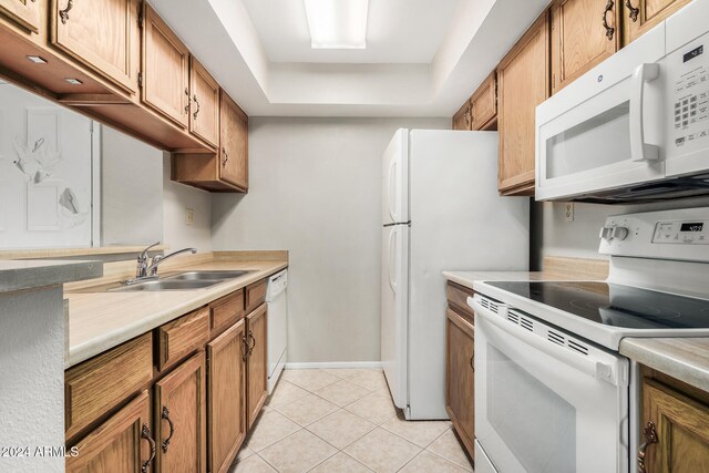 kitchen featuring a tray ceiling, sink, light tile patterned floors, and white appliances