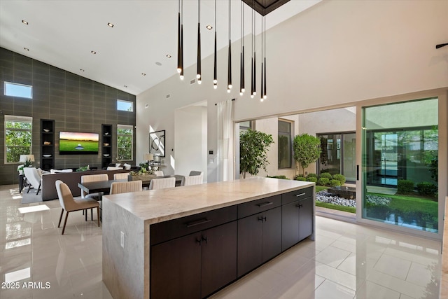 kitchen with high vaulted ceiling, open floor plan, light tile patterned floors, light stone counters, and a kitchen island