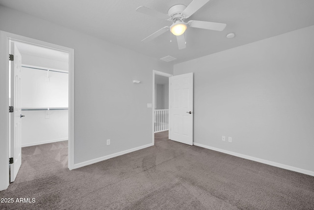 unfurnished bedroom featuring a spacious closet, baseboards, carpet flooring, a closet, and a ceiling fan