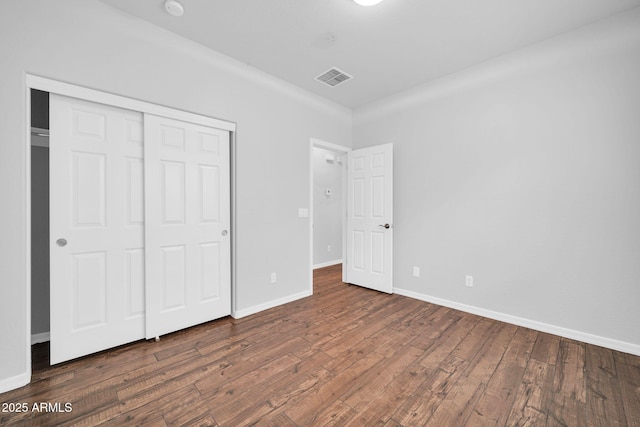 unfurnished bedroom featuring visible vents, wood-type flooring, baseboards, and a closet