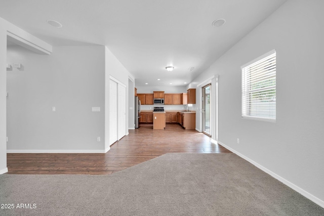 unfurnished living room featuring recessed lighting, light colored carpet, light wood-type flooring, and baseboards