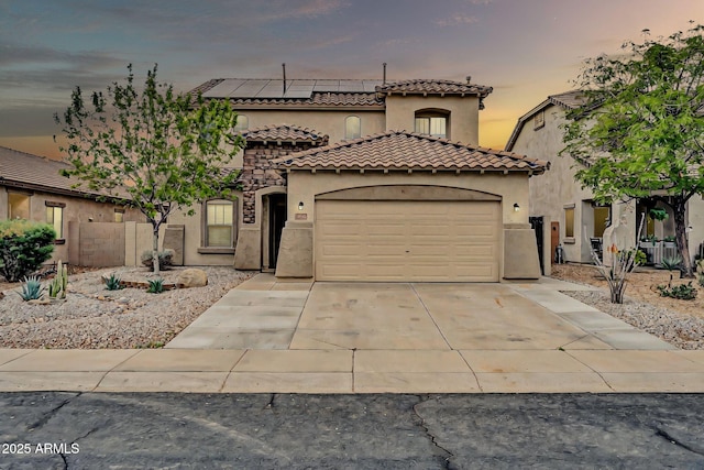 mediterranean / spanish home featuring driveway, an attached garage, stucco siding, a tile roof, and roof mounted solar panels