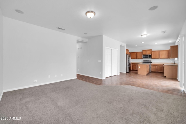 unfurnished living room featuring baseboards, carpet, visible vents, and a sink