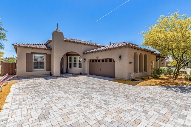 mediterranean / spanish-style home with a tiled roof, decorative driveway, fence, an attached garage, and stucco siding
