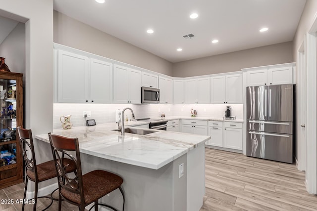 kitchen with white cabinets, light stone counters, stainless steel appliances, a peninsula, and visible vents