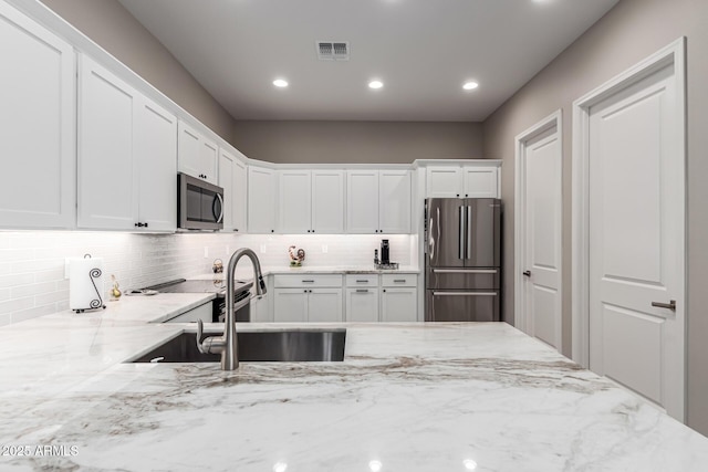 kitchen with backsplash, a sink, light stone counters, white cabinets, and stainless steel appliances