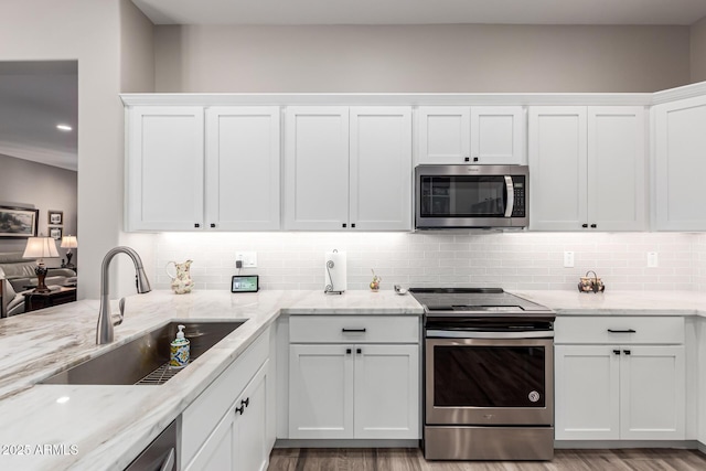 kitchen with white cabinets, stainless steel appliances, light stone countertops, and a sink