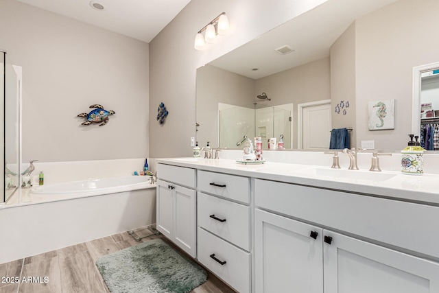 full bath featuring a sink, double vanity, wood finished floors, a garden tub, and a stall shower