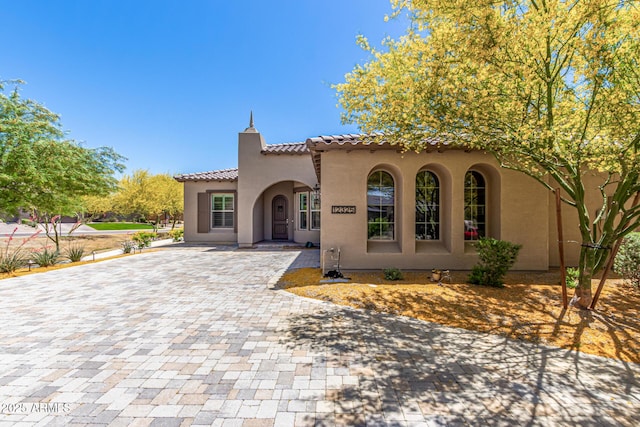 mediterranean / spanish-style house featuring decorative driveway, stucco siding, and a tiled roof