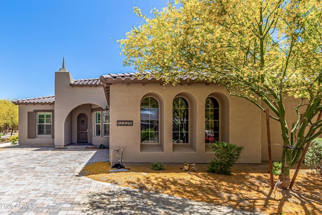 mediterranean / spanish-style house with a tiled roof, decorative driveway, and stucco siding