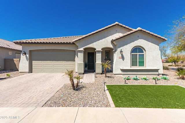 mediterranean / spanish house with stucco siding, decorative driveway, a front yard, a tile roof, and a garage