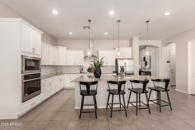 kitchen featuring decorative backsplash, appliances with stainless steel finishes, an island with sink, and wall chimney range hood