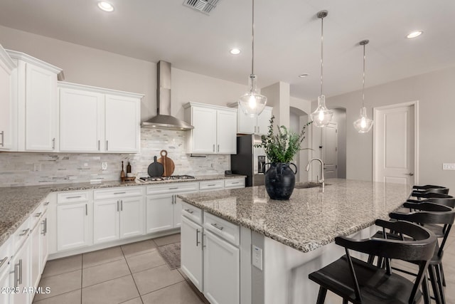 kitchen featuring wall chimney exhaust hood, a kitchen breakfast bar, white cabinets, stainless steel appliances, and backsplash