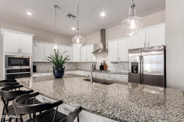 kitchen featuring tasteful backsplash, visible vents, a sink, wall chimney range hood, and appliances with stainless steel finishes