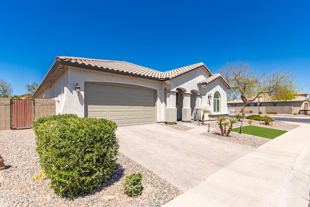 mediterranean / spanish-style home featuring a garage, stucco siding, a tiled roof, and decorative driveway