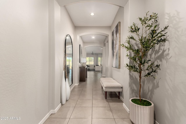 hall with light tile patterned floors, baseboards, recessed lighting, and arched walkways