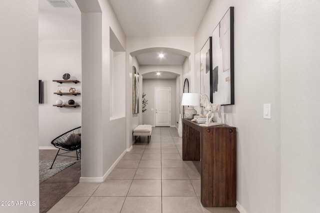 corridor featuring arched walkways, visible vents, baseboards, and light tile patterned flooring