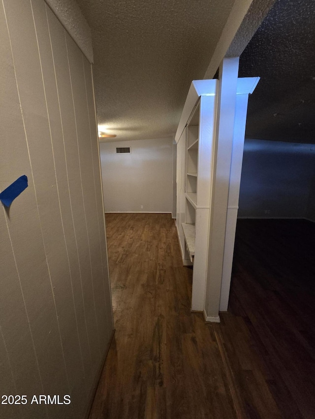 hall featuring a textured ceiling, wood finished floors, and visible vents