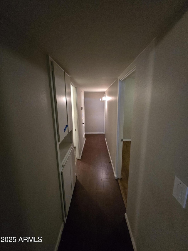 corridor featuring dark wood-style flooring and baseboards