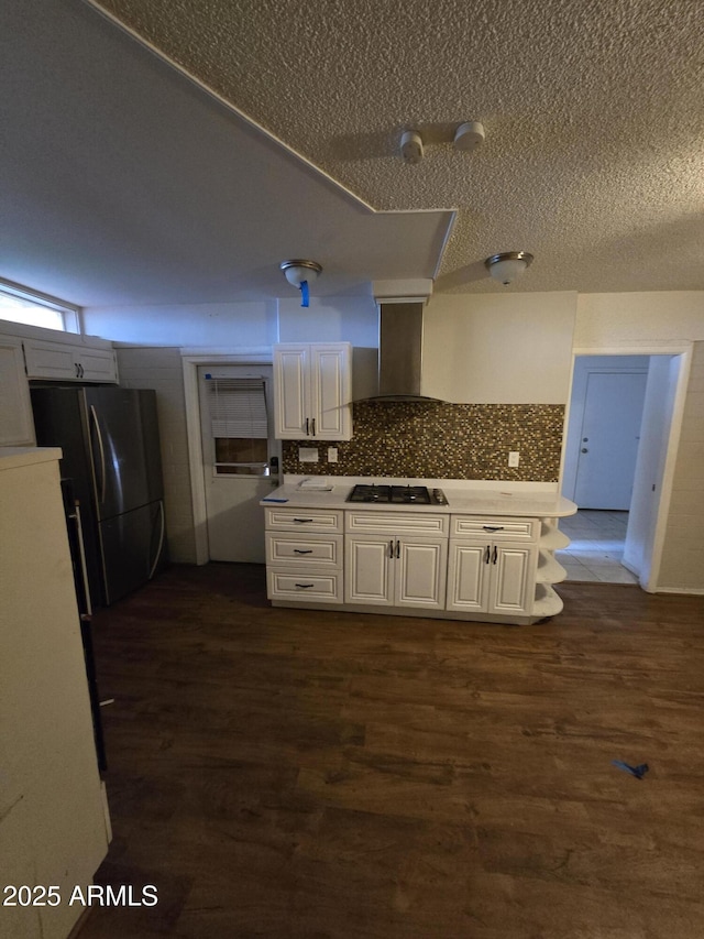 kitchen featuring dark wood-type flooring, gas stovetop, white cabinets, wall chimney range hood, and freestanding refrigerator