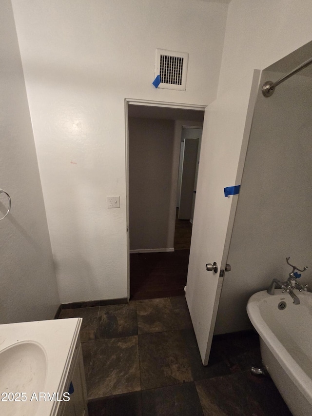 full bath featuring a tub to relax in, visible vents, stone finish flooring, vanity, and baseboards