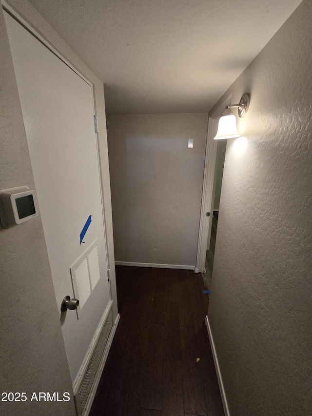 corridor featuring a textured wall, wood finished floors, visible vents, and baseboards