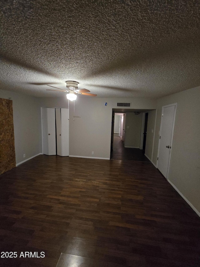 empty room with a textured ceiling, ceiling fan, wood finished floors, and visible vents