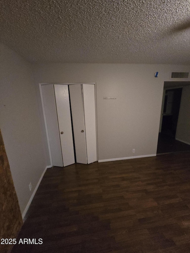 spare room featuring a textured ceiling, wood finished floors, visible vents, and baseboards