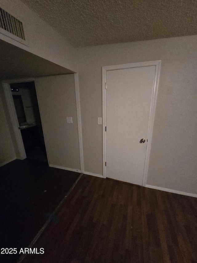 interior space featuring a textured ceiling, dark wood-style flooring, visible vents, and baseboards