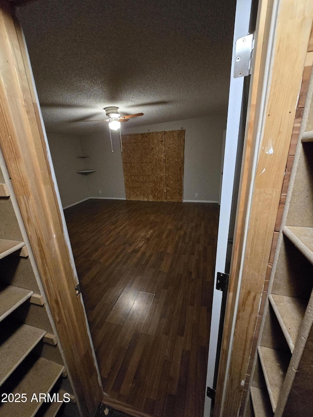 empty room with a textured ceiling, wood finished floors, stairs, and a ceiling fan