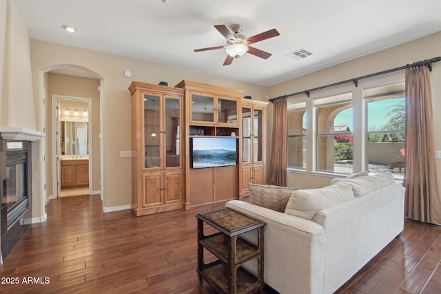 9305 E Canyon View Rd, Scottsdale, AZ 85255 - living room featuring baseboards, ceiling fan, arched walkways, a glass covered fireplace, and dark wood-style flooring