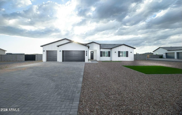 modern inspired farmhouse with a garage, decorative driveway, fence, and board and batten siding