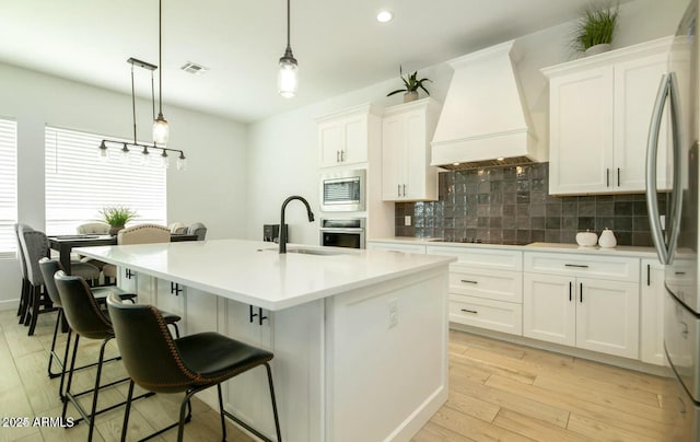 kitchen with visible vents, custom range hood, a sink, stainless steel appliances, and decorative backsplash