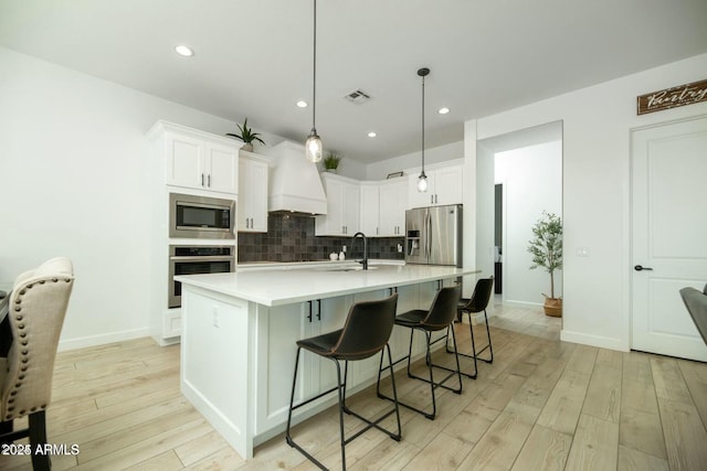 kitchen with tasteful backsplash, visible vents, premium range hood, light wood-style flooring, and stainless steel appliances