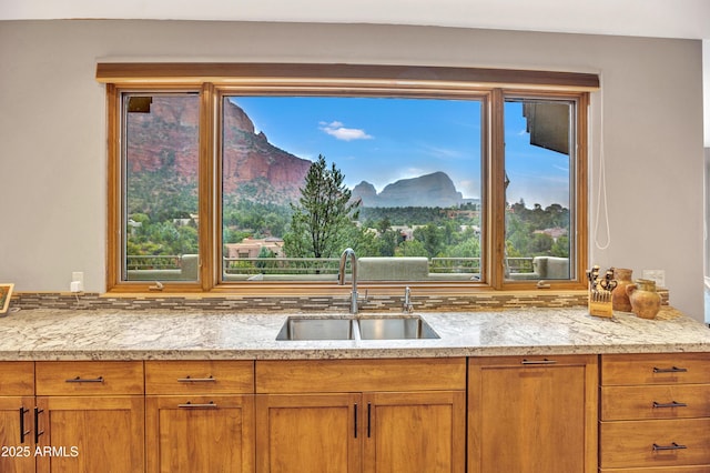kitchen featuring brown cabinetry, light stone countertops, a sink, and a mountain view