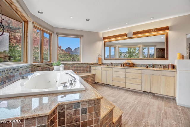 bathroom with a sink, double vanity, a tub with jets, and a healthy amount of sunlight