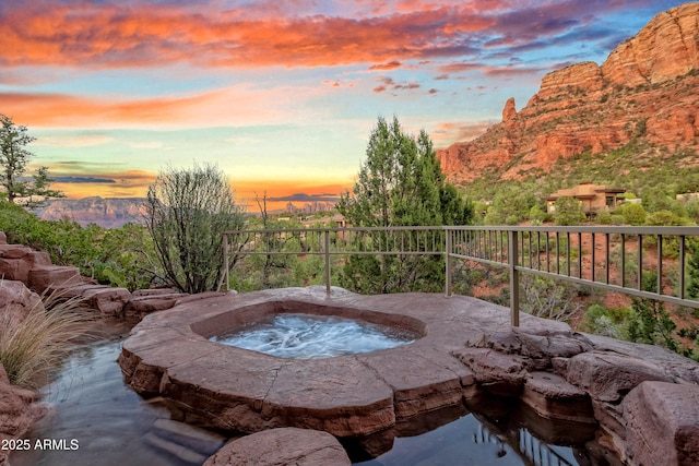 pool at dusk featuring a mountain view, fence, and an in ground hot tub