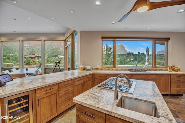 kitchen featuring brown cabinets, beverage cooler, a sink, and light stone counters