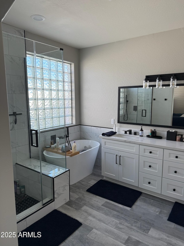 bathroom with vanity, independent shower and bath, hardwood / wood-style floors, and tile walls