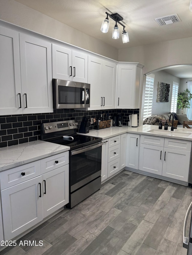 kitchen featuring sink, hardwood / wood-style flooring, appliances with stainless steel finishes, white cabinets, and decorative backsplash