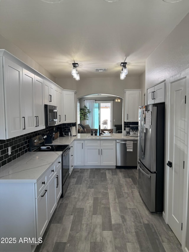 kitchen featuring white cabinetry, backsplash, stainless steel appliances, light stone counters, and wood-type flooring