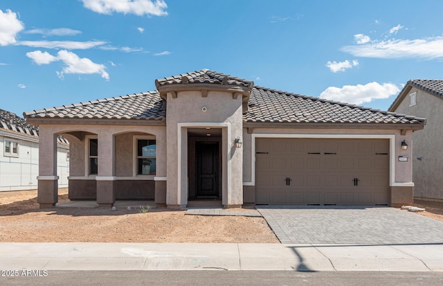 mediterranean / spanish-style home featuring an attached garage, a tiled roof, decorative driveway, and stucco siding