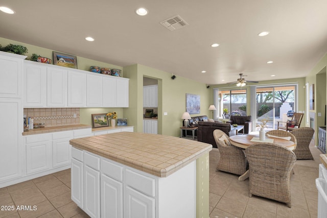 kitchen with ceiling fan, tile counters, a kitchen island, decorative backsplash, and white cabinets