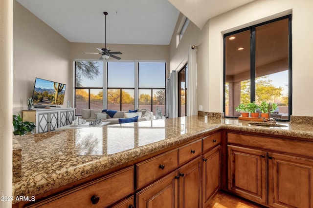 kitchen with ceiling fan, light stone counters, and sink