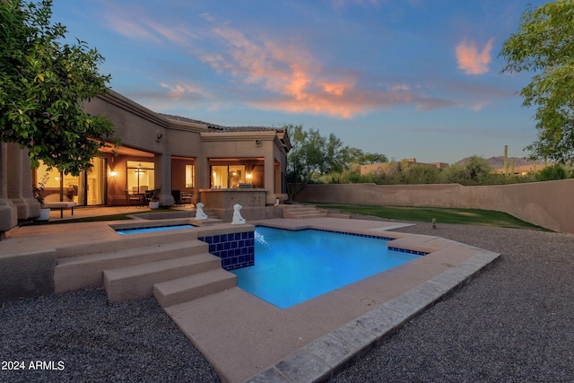 pool at dusk with an in ground hot tub, exterior kitchen, and a patio