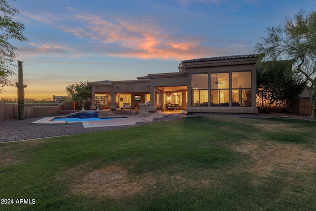 back house at dusk with a patio area, a yard, and a fenced in pool