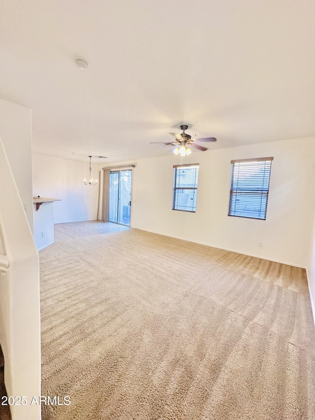 spare room featuring carpet flooring and ceiling fan with notable chandelier