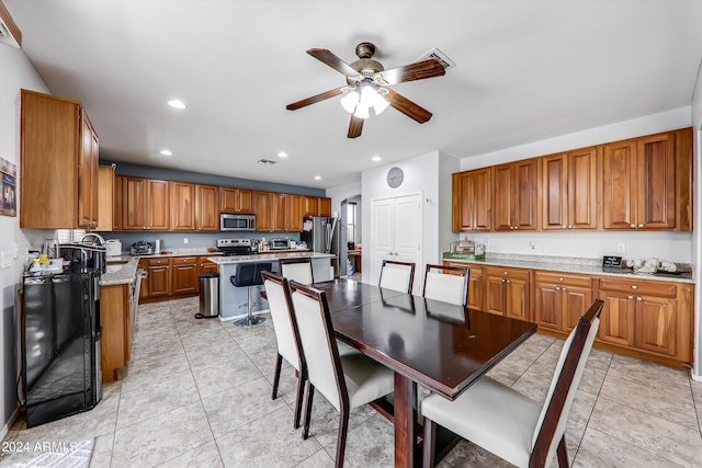 kitchen with light stone countertops, appliances with stainless steel finishes, a center island, light tile patterned flooring, and ceiling fan