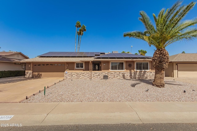 ranch-style house featuring a garage, driveway, solar panels, stone siding, and stucco siding