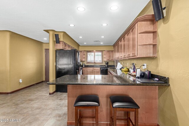 kitchen featuring baseboards, dark stone countertops, a peninsula, black appliances, and open shelves